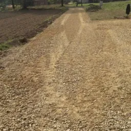 Przygotowanie podłoża z tłucznia pod drogę dojazdową na terenie wiejskim, widoczne ślady opon i wyrównany teren.