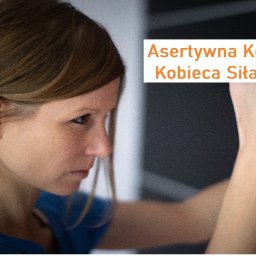 Grażyna Arendt GRAGA - Kobieta z włosami związanymi w kucyk, z zamyślonym spojrzeniem, w trakcie zajęć z asertywności, z tekstem 'Asertywna Kobieta - Kobieca Siła i Moc' nałożonym na obraz.