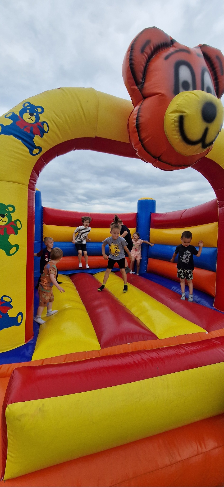 Radosne dzieci skaczą w dmuchanym zamku w Szczecinie. Kolorowy zamek z motywem misia, pełen energii i zabawy. Idealne rozwiązanie na imprezy plenerowe.