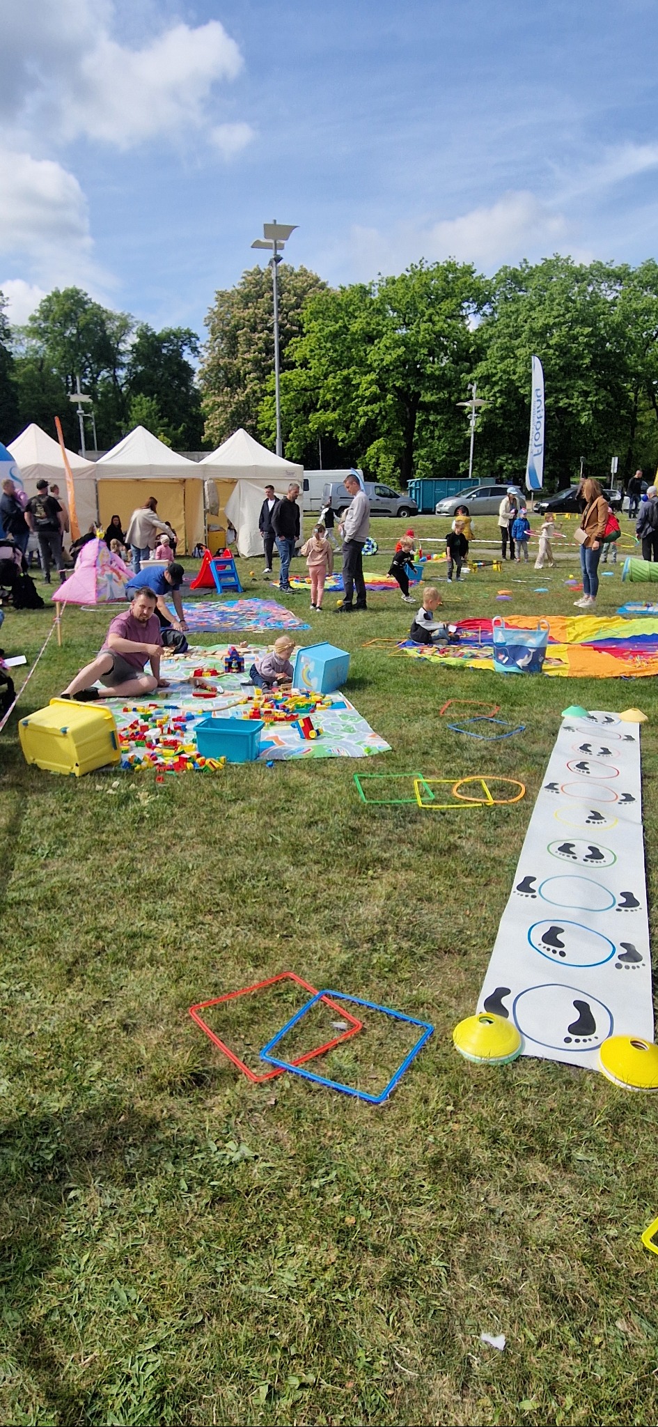 Plenerowa impreza dla dzieci: animatorzy, dmuchańce, gry na trawie, kolorowe rekwizyty, dzieci bawiące się pod opieką dorosłych w słoneczny dzień.