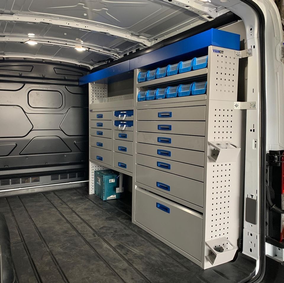 Wnętrze furgonetki z zamontowanym systemem regałów i szuflad marki Vankit, z niebieskimi akcentami, widoczne narzędzia w tle.