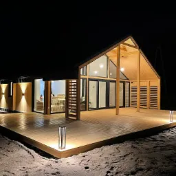 Nowoczesny dom z drewna z dużym tarasem oświetlonym lampami podłogowymi, widok nocą.