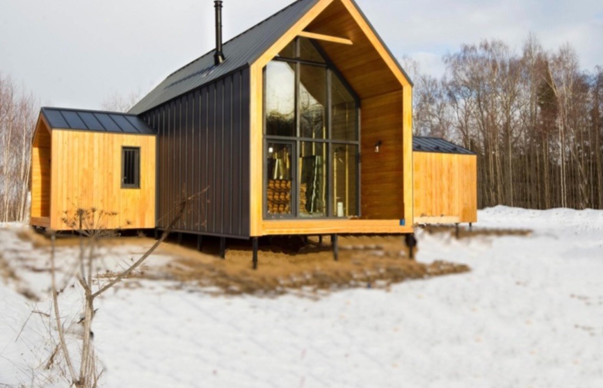 Nowoczesny dom z drewnianą elewacją i dużym przeszkleniem, posadowiony na słupach, otoczony śnieżnym krajobrazem.