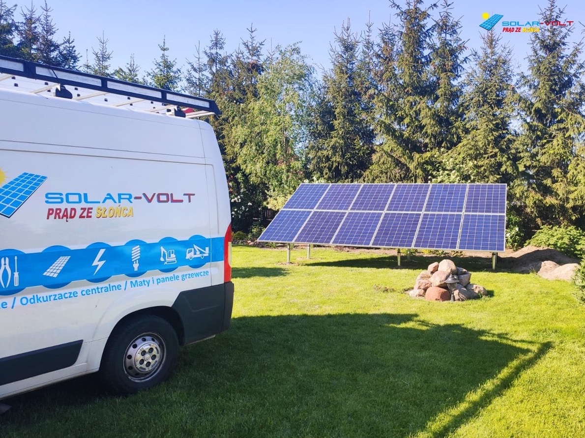 Instalacja paneli słonecznych na trawniku przed domem, widoczny samochód dostawczy z logo firmy Solar-Volt i narzędziami na dachu.