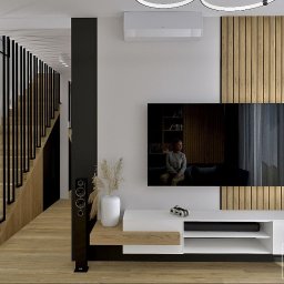 DG Projekty Wnętrz Diana Grabowska - Wizualizacja salonu z drewnianą ścianą, schodami z czarną balustradą i białymi meblami. Na ekranie telewizora widoczna osoba siedząca na kanapie.