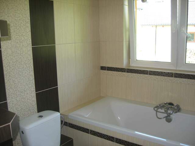 Ukończona łazienka z beżowymi i brązowymi płytkami, widoczna wanna, toaleta i okno z widokiem na zewnątrz.