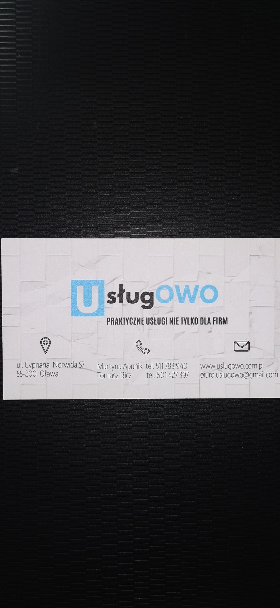 Wizytówka firmy Usługowo z adresem, numerami telefonów i adresem email, na ciemnym tle.