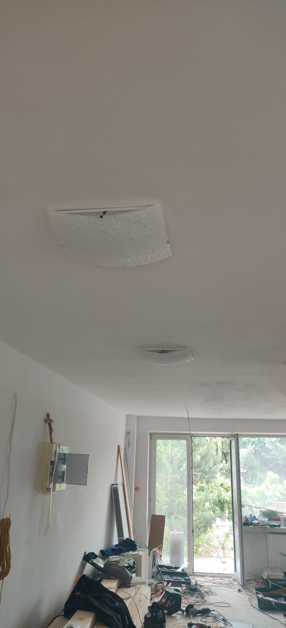 Dwa identyczne, kwadratowe plafony z dekoracyjnym szkłem zamontowane na białym suficie w trakcie remontu, z widocznymi przewodami i bałaganem na podłodze.