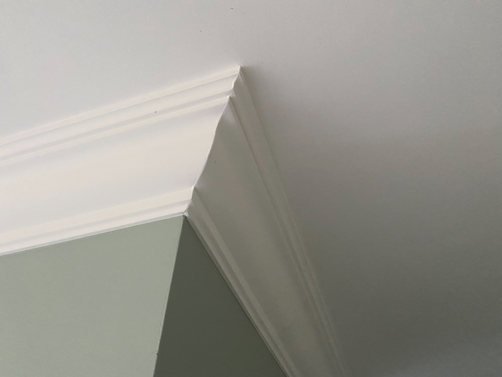 Szczegółowe ujęcie narożnika ściany i sufitu z listwą ozdobną, świeżo pomalowane na biało, z delikatnym odcieniem zieleni na ścianie.