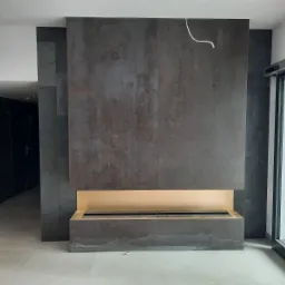 Nowoczesny kominek bio w obudowie z ciemnego kamienia, z widoczną wnęką na palenisko i fragmentem podłogi z szarych płytek.