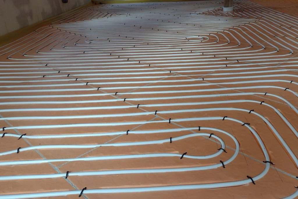 Rozłożone rury ogrzewania podłogowego na izolacji, zabezpieczone czarnymi uchwytami, widok z góry na dużej powierzchni.