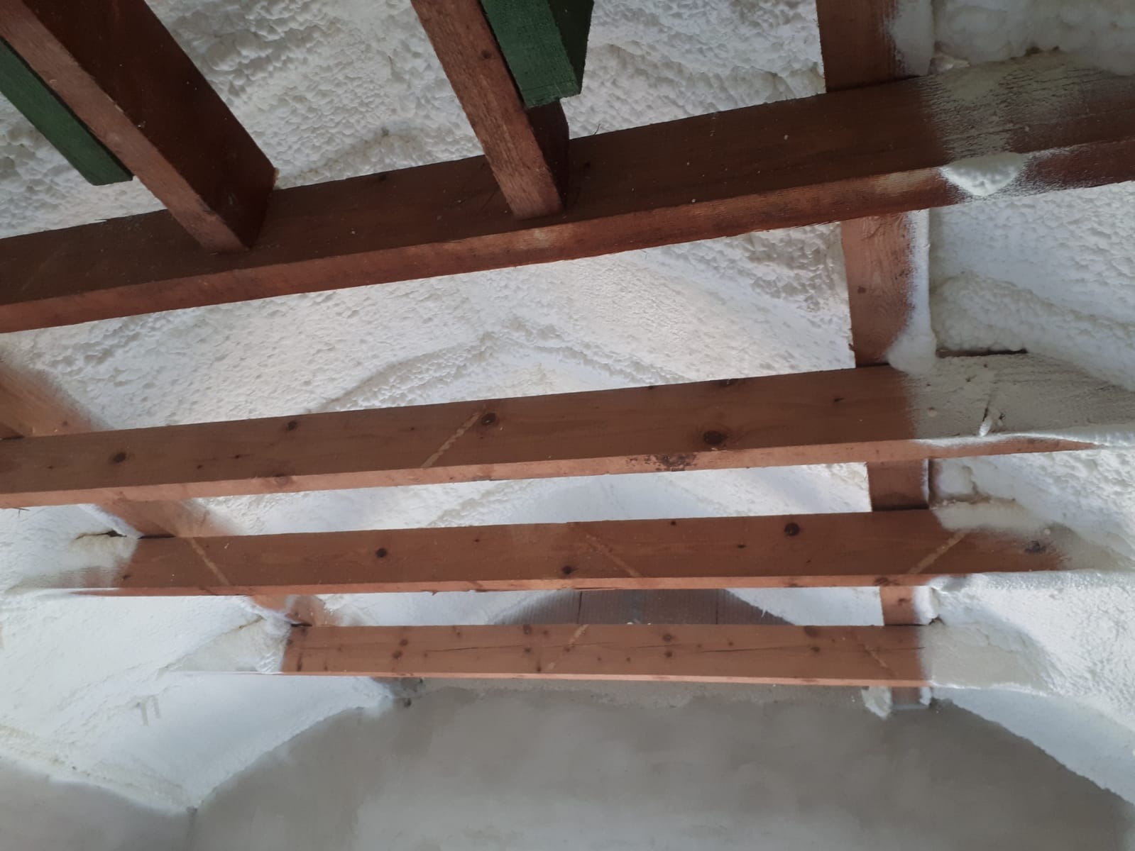 Poddasze ocieplone białą pianką izolacyjną między drewnianymi belkami stropowymi w Warszawie.