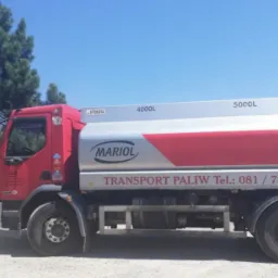 Czerwona cysterna z napisem 'TRANSPORT PALIW' i logo 'MARIOL' na tle zielonych drzew i błękitnego nieba. Zbiornik cysterny oznaczony pojemnościami 3000L, 4000L, 5000L oraz symbolami ostrzegawczymi.