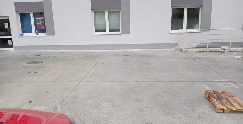 Świeżo pomalowany budynek biurowy w odcieniach szarości, z widocznymi śladami po malowaniu na betonowym podłożu i paletą malarską w rogu.