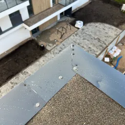 Szczegółowe ujęcie krawędzi dachu pokrytego papą z metalowym obrzeżem mocowanym na nity, na tle nowego budynku i przygotowanego terenu.