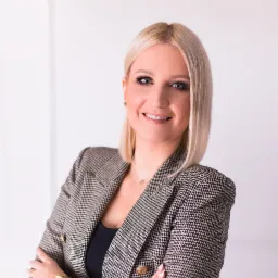 Portret uśmiechniętej blondynki w tweedowej marynarce z podwiniętymi rękawami, na białym tle.