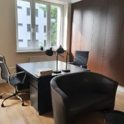 Nowoczesne biuro prawnicze z czarnym biurkiem, skórzanym fotelem klubowym i lampkami w stylu retro, widok na budynek z oknem.