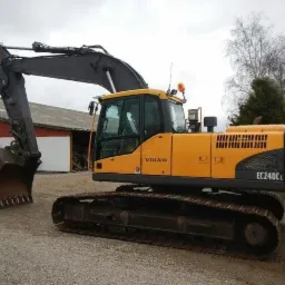 Żółta koparka gąsienicowa Volvo EC240CL zaparkowana na żwirowym placu, widok z boku, z podniesionym ramieniem i łyżką skierowaną w lewo.