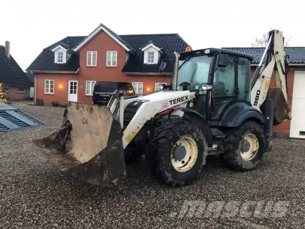 Biało-czarna koparko-ładowarka Terex 980 Elite z brudną łyżką z przodu, zaparkowana na żwirowym podłożu przed ceglanym domem z czerwonymi oknami.