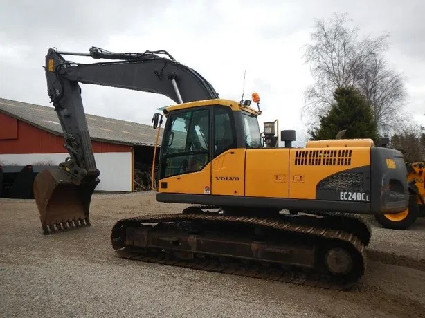 Żółta koparka gąsienicowa Volvo EC240CL zaparkowana na żwirowym placu, widok z boku, z podniesionym ramieniem i łyżką skierowaną w lewo.