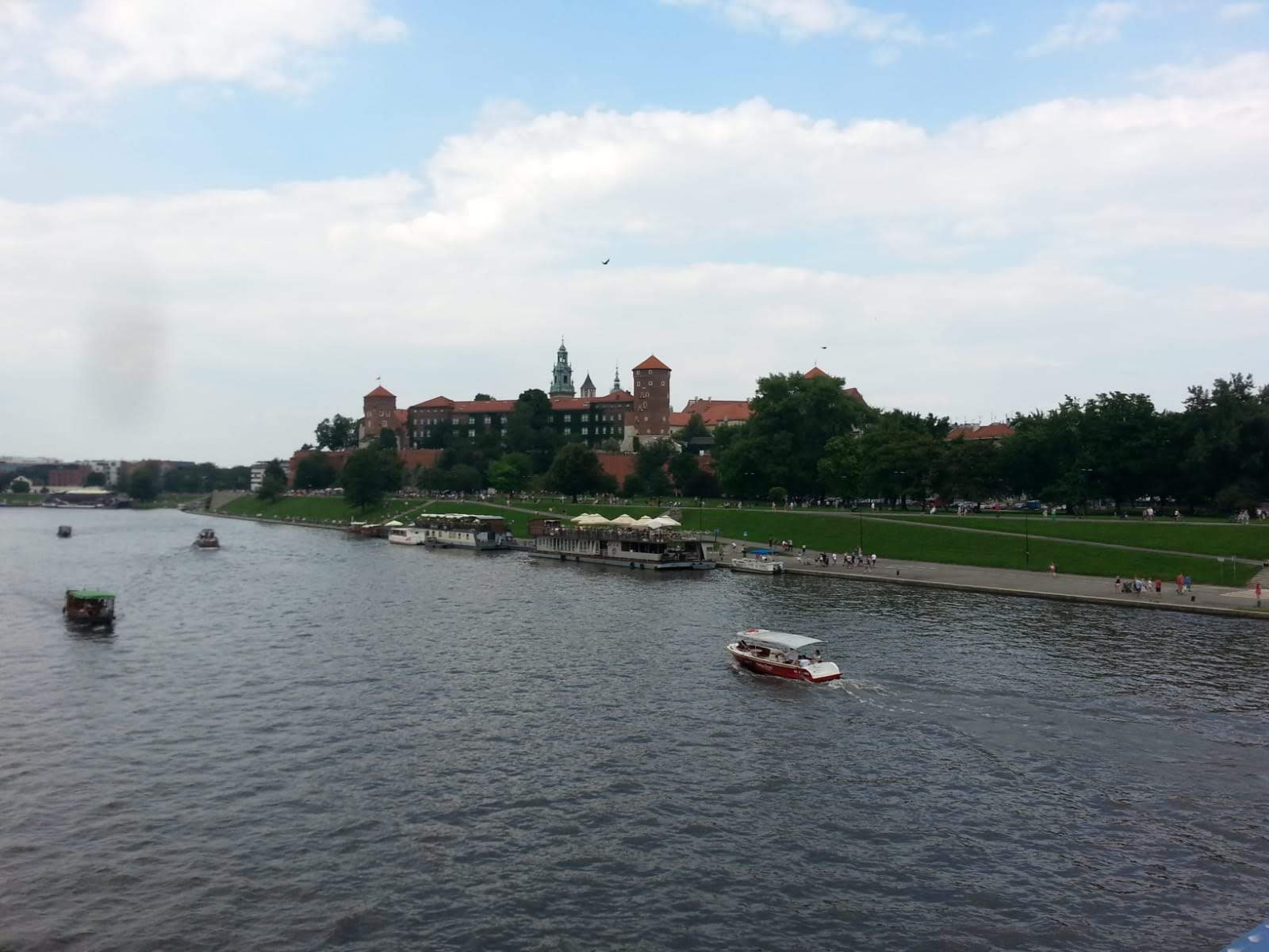 Panorama Krakowa z rzeki Wisły, z widocznym Wawelem, bulwarami i pływającymi łodziami.