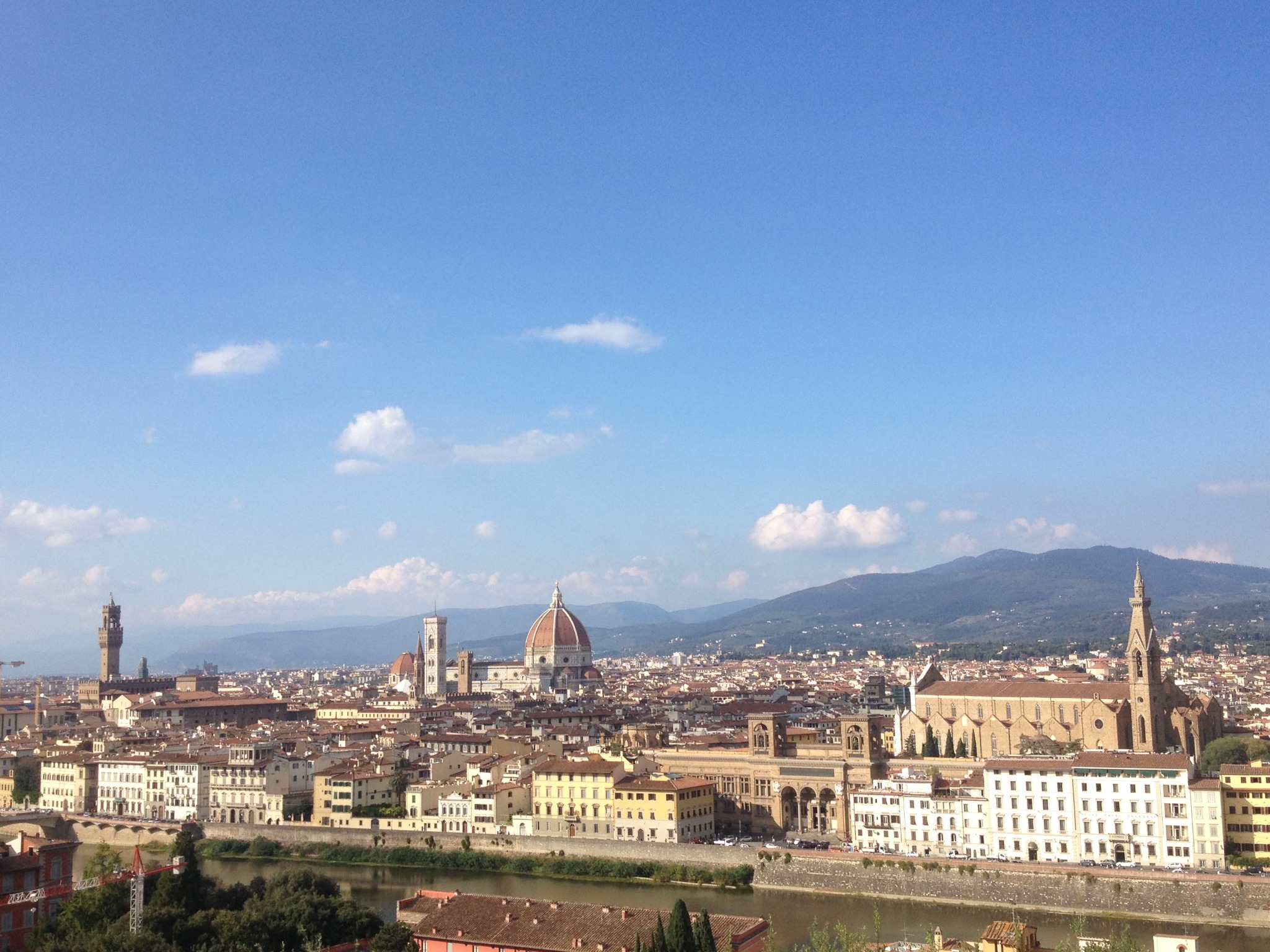 Panoramiczny widok na Florencję z rzeką Arno, katedrą Santa Maria del Fiore i toskańskimi wzgórzami w tle, uchwycony w jasnym, słonecznym dniu.