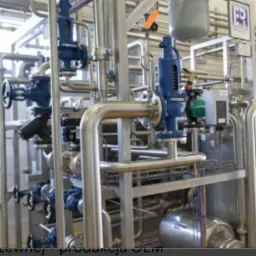 Złożona instalacja przemysłowa z rurami ze stali nierdzewnej, zaworami i manometrami, widoczne zbiorniki ciśnieniowe i pompy, całość w jasnym, przemysłowym otoczeniu.
