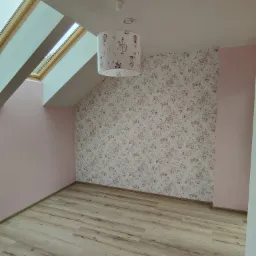 Pokój na poddaszu po remoncie: jasne panele podłogowe, ściana w kwiatowe tapety, różowa ściana, okno dachowe i lampa z motywem dziecięcym.