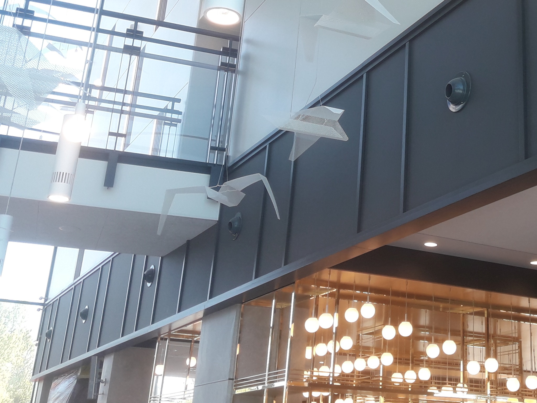 Wnętrze nowoczesnego biura z instalacją wentylacyjną na ścianie i dekoracyjnymi elementami pod sufitem, w tym lampami i ozdobami w kształcie ptaków.