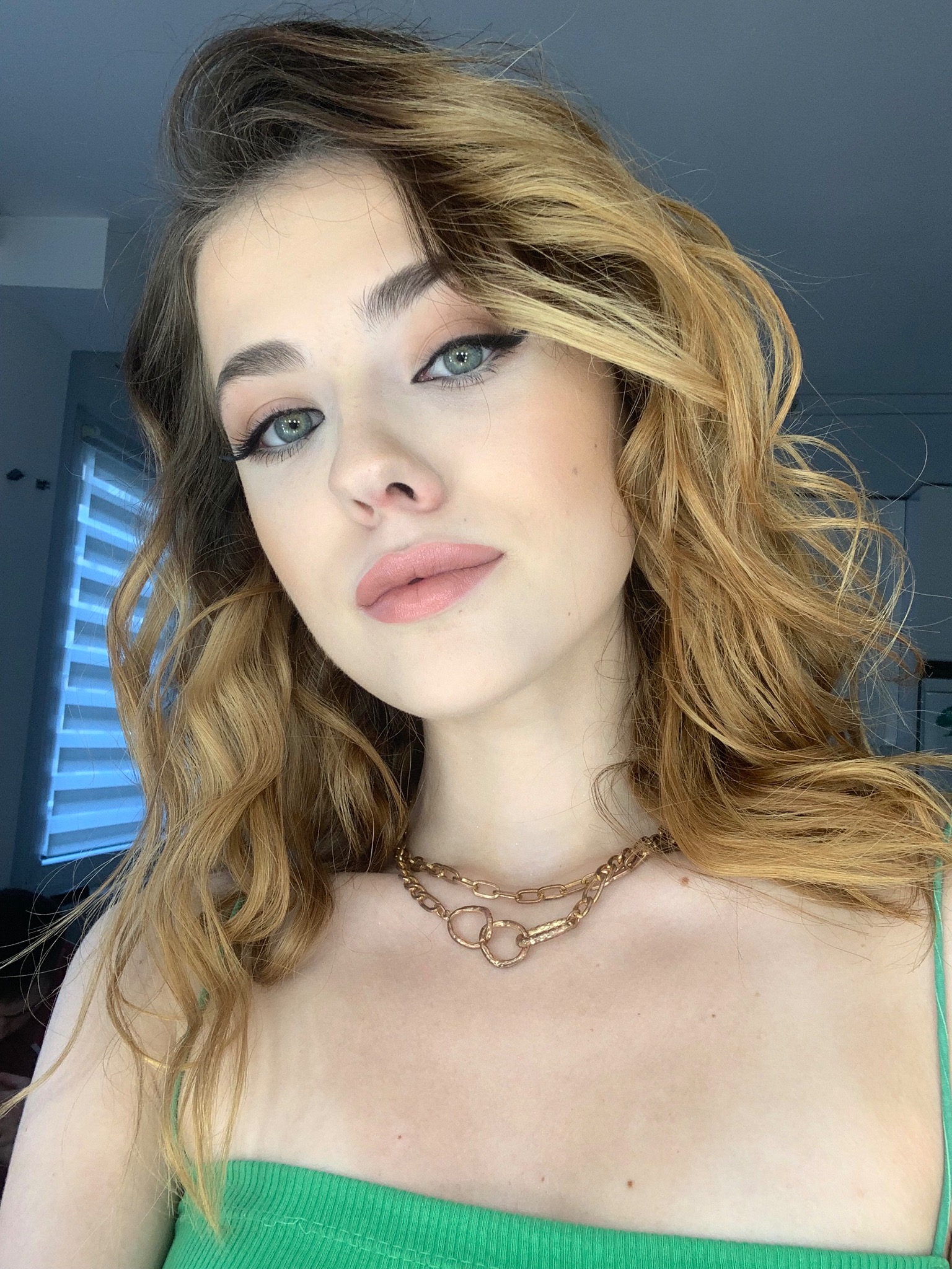 Portret młodej kobiety z profesjonalnie wykonanym makijażem: delikatne cienie, podkreślone oczy eyelinerem i pomadka w odcieniu nude, włosy w odcieniach blondu i brązu, stylizowane na luźne fale...