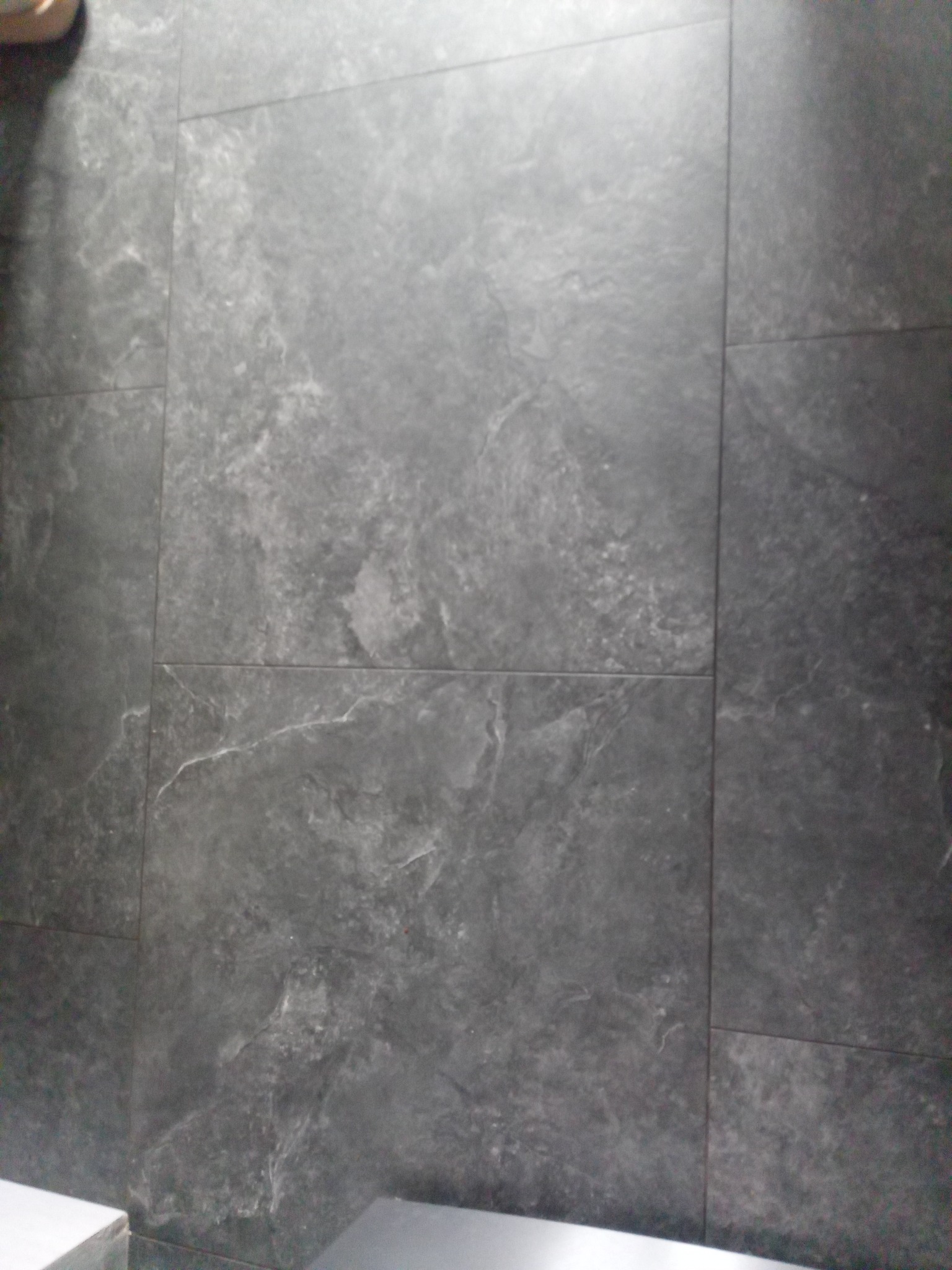 Matowe, grafitowe płytki imitujące kamień, ułożone z minimalną fugą, widoczne z bliska w słabym oświetleniu.