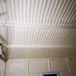 Poddasze ocieplone pianką, widoczne równomierne pokrycie stropu i ścian z uwzględnieniem ramy okiennej. Charakterystyczna struktura pianki na powierzchni.