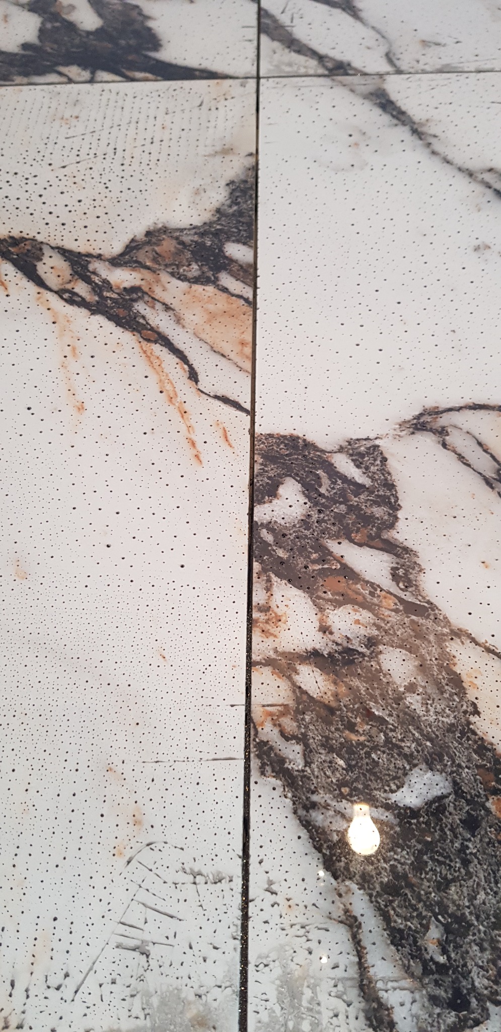 Płytki podłogowe imitujące marmur z wyraźnym wzorem żyłkowania, widoczne ślady po czyszczeniu, odbicie światła na powierzchni.