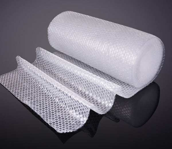 Rolka przezroczystej folii bąbelkowej, częściowo rozwinięta, prezentowana na błyszczącym, ciemnym tle z widocznym odbiciem.