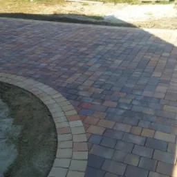 Nowo ułożona, wielobarwna kostka brukowa z obrzeżem w kształcie łuku, worki z materiałami budowlanymi w tle.