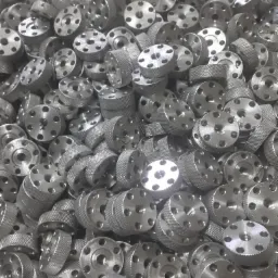 Stalowe, okrągłe elementy z otworami i radełkowaną krawędzią, ułożone w dużym zbiorze.