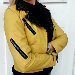 Żółta skórzana kurtka typu biker z czarną perforowaną podszewką, widoczny zegarek na nadgarstku.