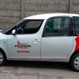 Srebrny samochód dostawczy z czarnym logo 'Agregaty PexPool Plus' i czerwonym graficznym motywem skrzydeł na boku, zaparkowany na tle betonowego muru.