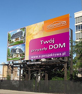 Billboard reklamujący domy jednorodzinne z logo 'Perspektywa' na tle błękitnego nieba i budynków miejskich.