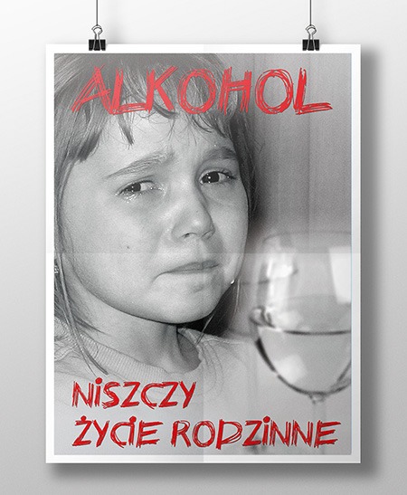 Plakat z czarno-białym zdjęciem płaczącej dziewczynki i kieliszkiem wina, z czerwonym napisem 'ALKOHOL NISZCZY ŻYCIE RODZINNE', wiszący na białej ścianie przypięty klamerkami.