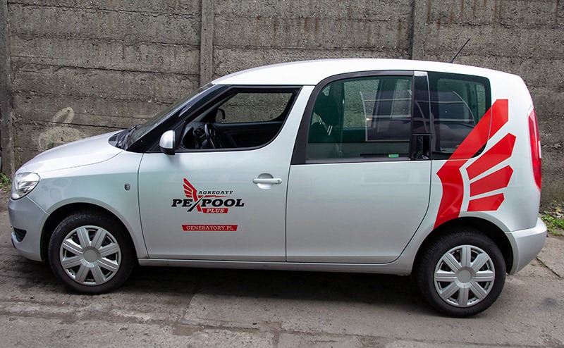Srebrny samochód dostawczy z czarnym logo 'Agregaty PexPool Plus' i czerwonym graficznym motywem skrzydeł na boku, zaparkowany na tle betonowego muru.