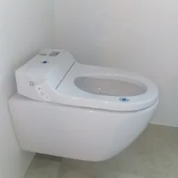 Wisząca toaleta myjąca z panelem sterowania, funkcją podgrzewania deski i automatycznym spłukiwaniem, zamontowana w minimalistycznej łazience z białymi płytkami.