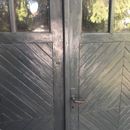 TiT Mariusz Bogusz - Szare, drewniane drzwi z ukośnym wzorem i małymi okienkami, przez które widać zieleń drzew