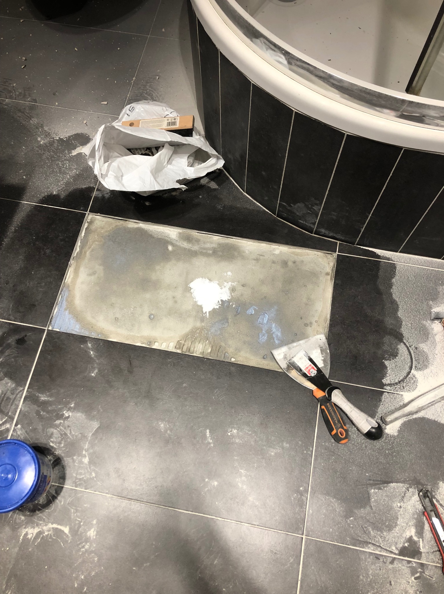 Przygotowanie podłoża pod nową płytkę podłogową w łazience, widoczna stara warstwa kleju, szpachelki i opakowanie po fugach