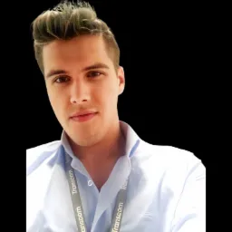 Portret młodego mężczyzny w błękitnej koszuli z identyfikatorem Transcom na smyczy, uśmiechającego się do kamery na czarnym tle.