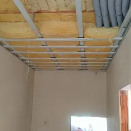 Montaż metalowej konstrukcji sufitu podwieszanego z widoczną izolacją z wełny mineralnej oraz rur wentylacyjnych, ściany przygotowane do dalszych prac wykończeniowych.