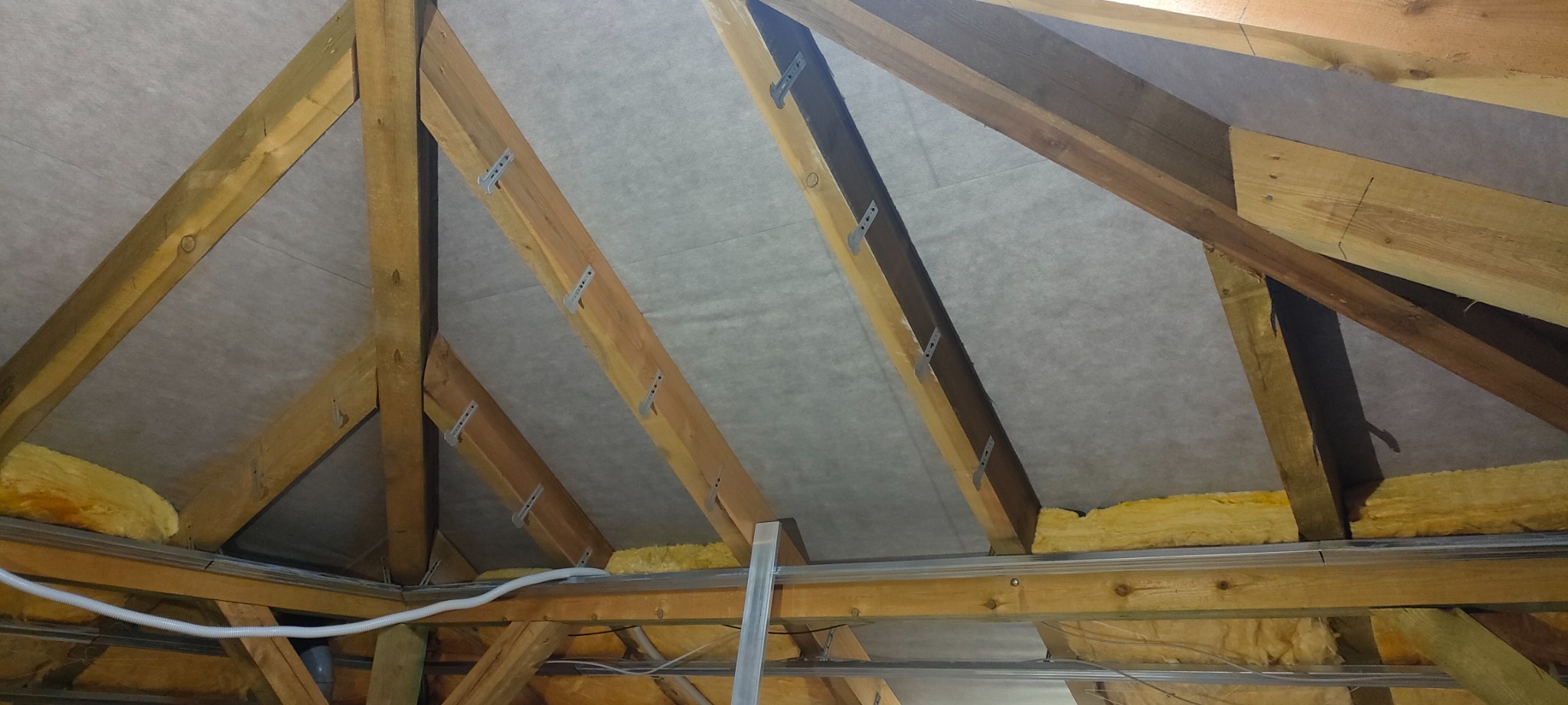 Konstrukcja drewniana poddasza z widoczną izolacją z wełny mineralnej i membraną paroizolacyjną mocowaną metalowymi uchwytami.
