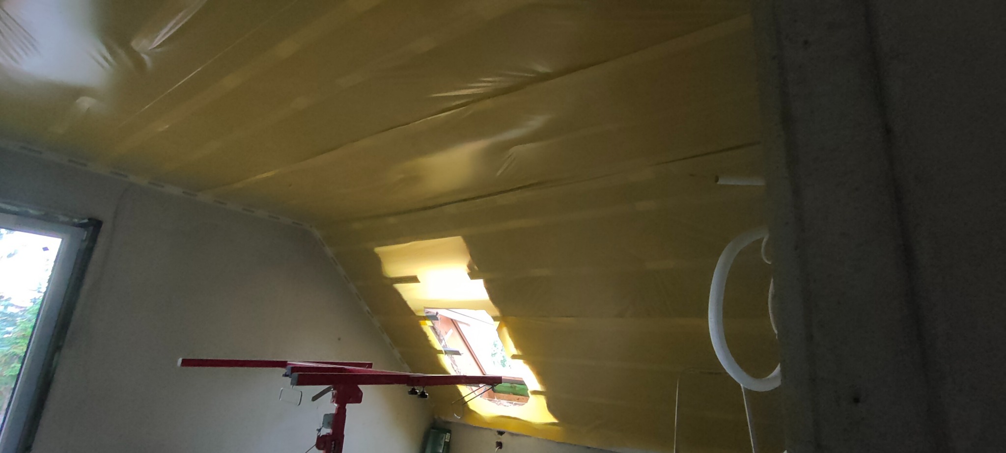 Ocieplone poddasze folią paroizolacyjną, widoczny fragment okna dachowego i podnośnik do płyt.