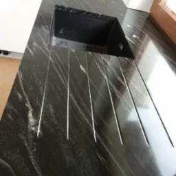 Czarny blat kamienny z wbudowanym zlewozmywakiem i ociekaczem w postaci wyżłobień, widoczne białe żyłki w kamieniu, ujęcie z góry.