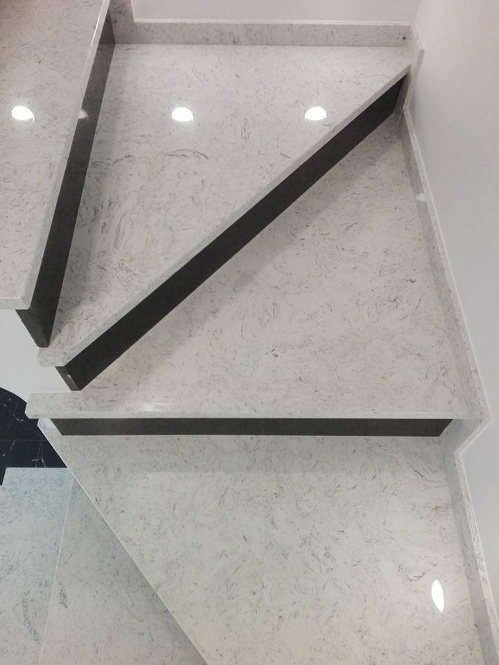 Schody wewnętrzne wykończone białym kamieniem z ciemnoszarymi podstopnicami, widok z góry na trzy stopnie.